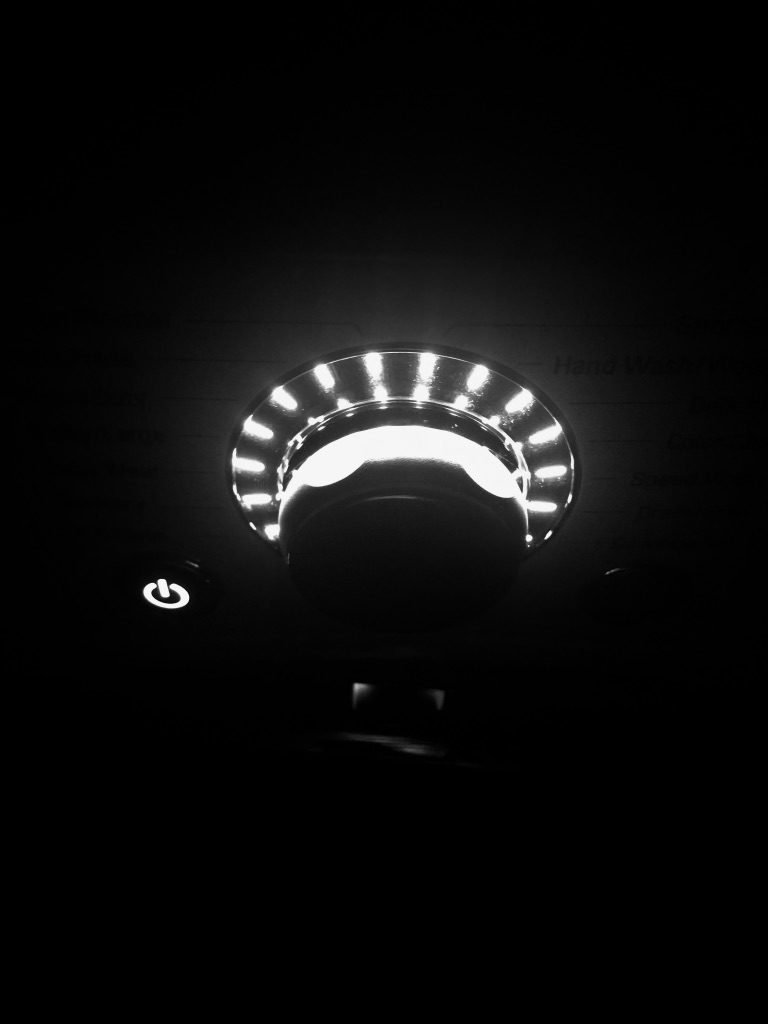 Black & White close up of light up washing machine power button and dial in dark room