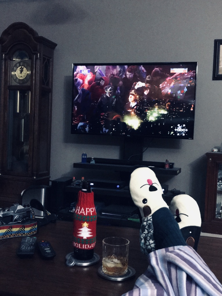 Feet up on coffee table with beer watching New Years celebration on TV.
