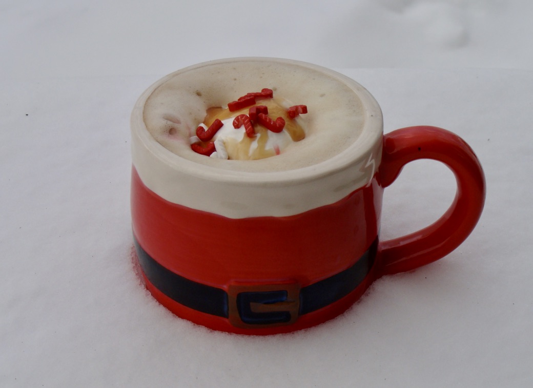 Santa coffee mug with frothy hot drink topped with whip cream and candy cane sprinkles