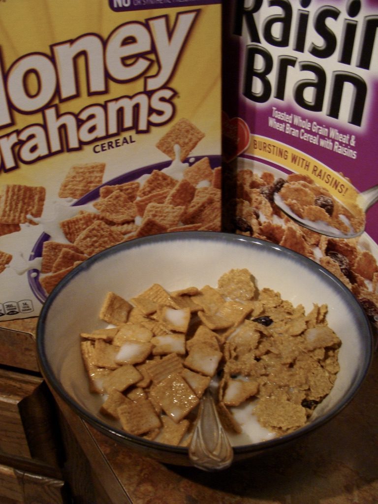 Honey Grahams and Raisin Bran cereal on a bowl with the cereal boxes behind