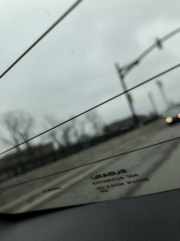 Looking out the back of a car window, SUBARU is backwards and in focus everything behind it is blurry and out of focus
