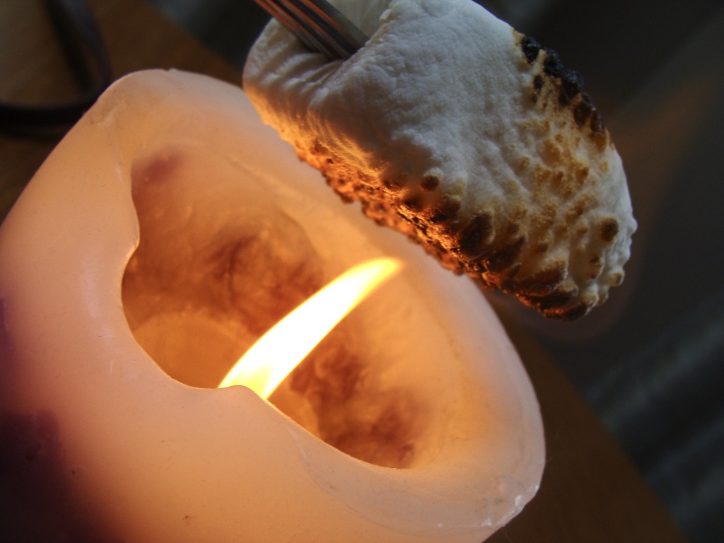 A marshmallow being toasted over a candle flame
