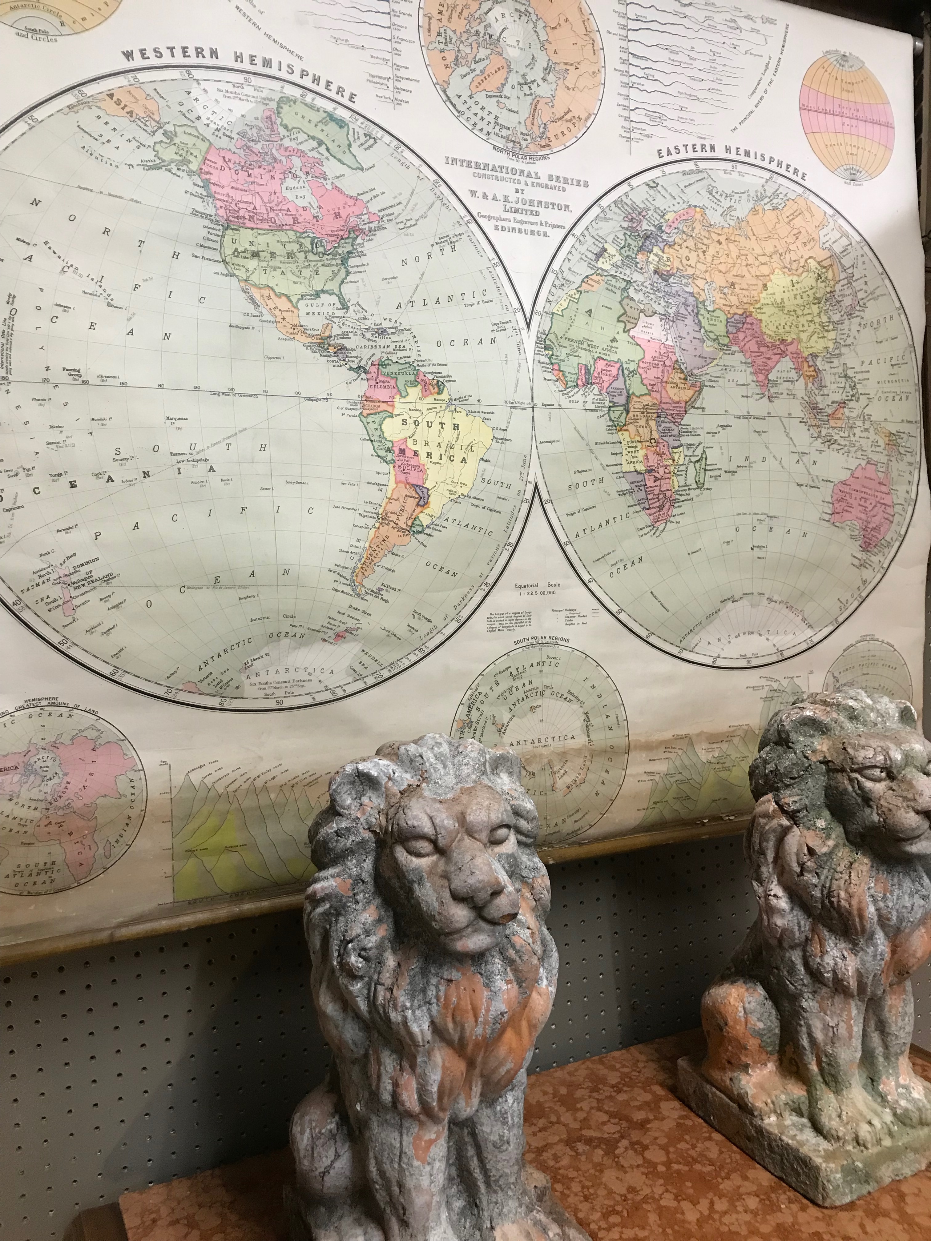 Map of world hanging on wall with 2 stone lions in front on table. 