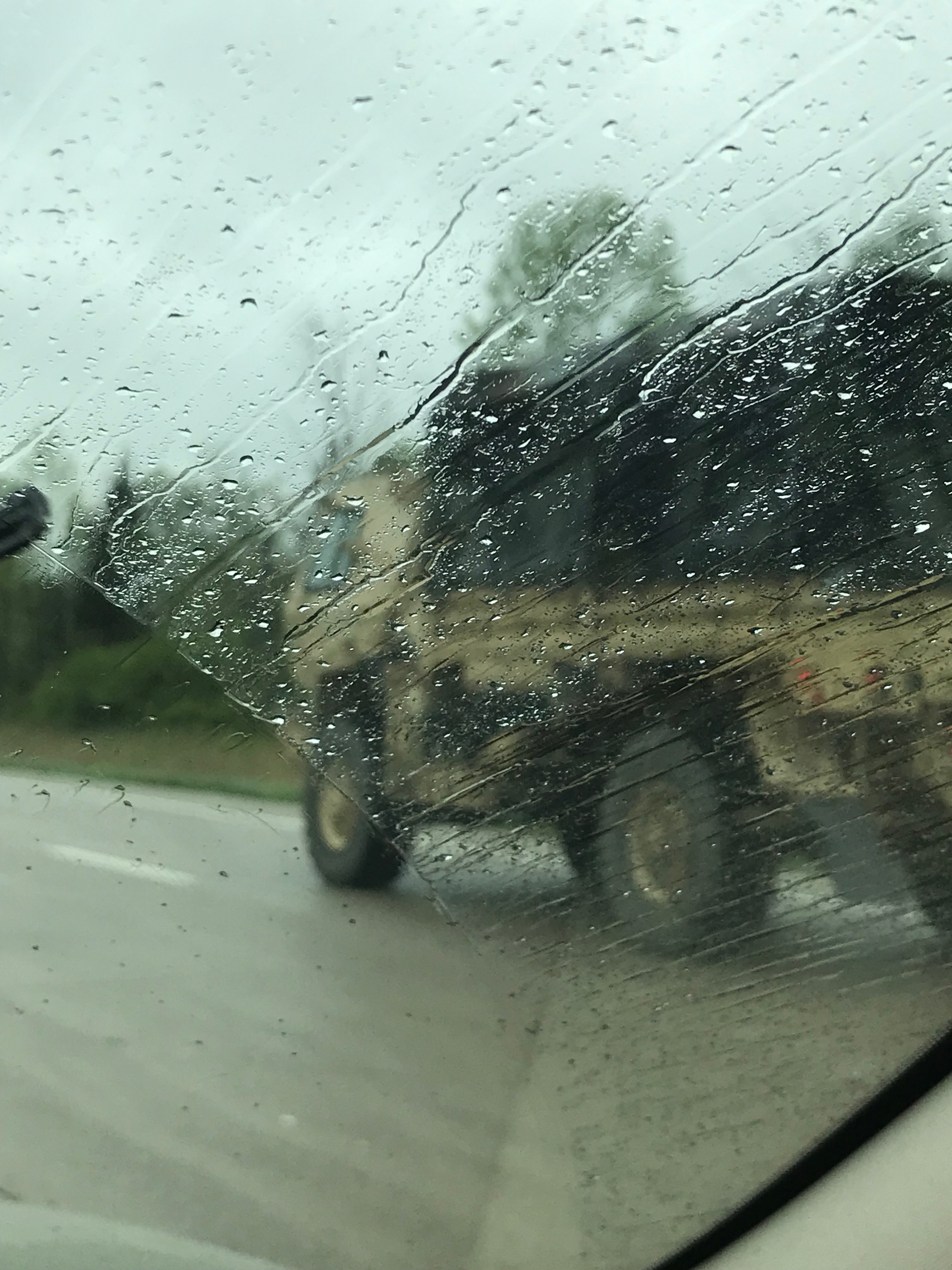 Rain on a windshield of a car with a blurry army truck on background. 
