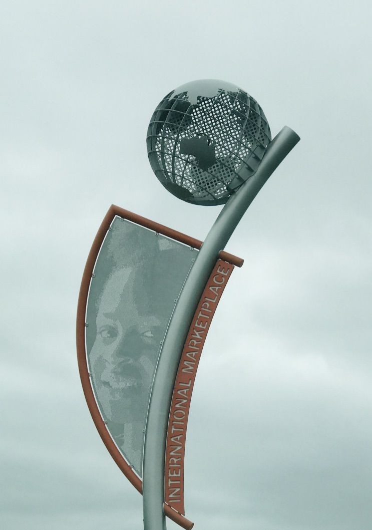 A metal globe at the top of a pole with a sign for the International Marketplace