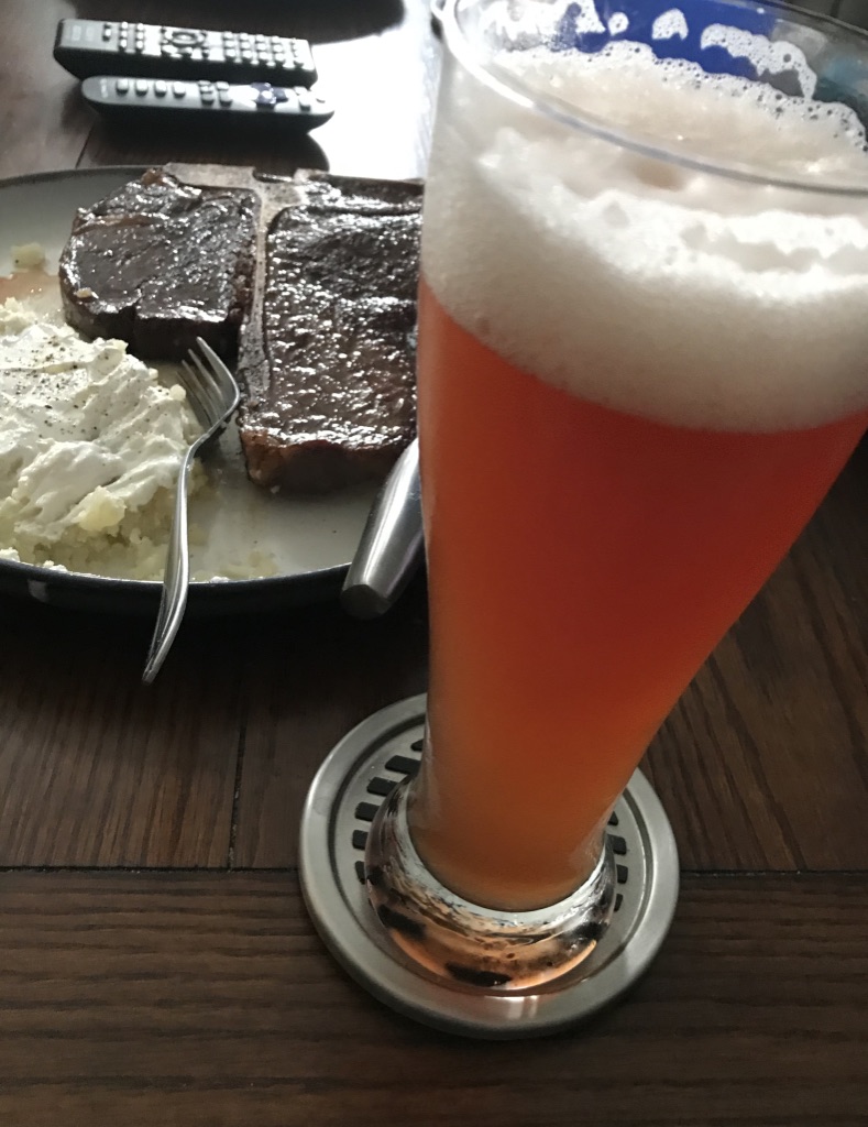 Beer in a tall beer glass with plate of steak and potato