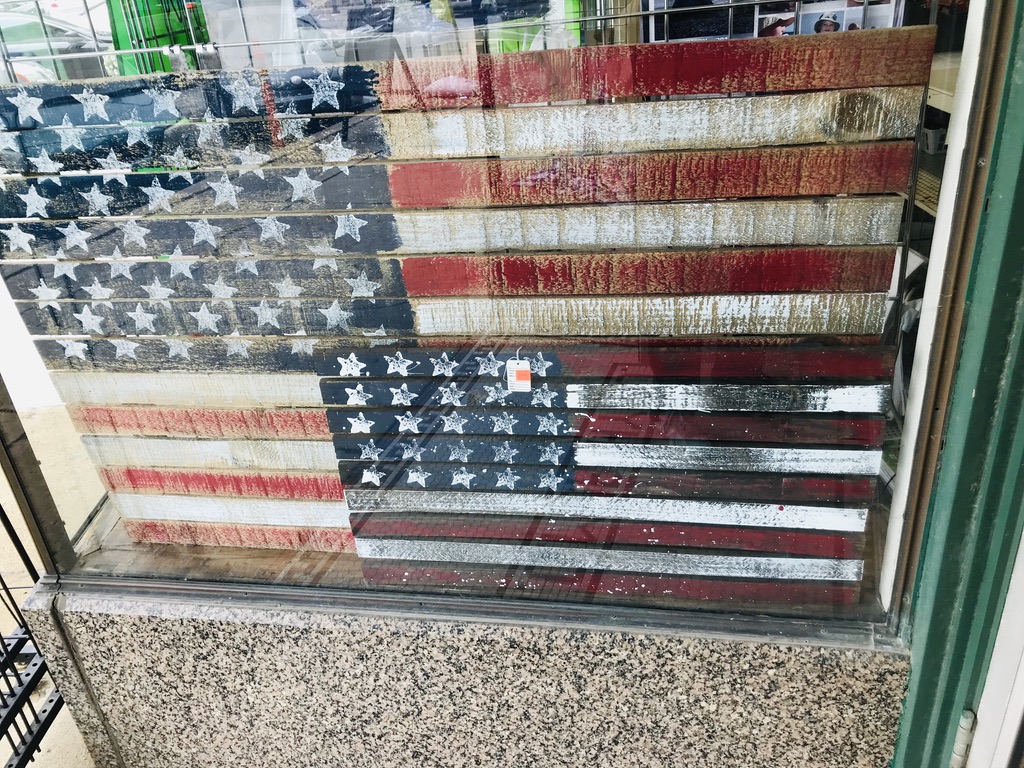 Wooden American flag shot through a store window.