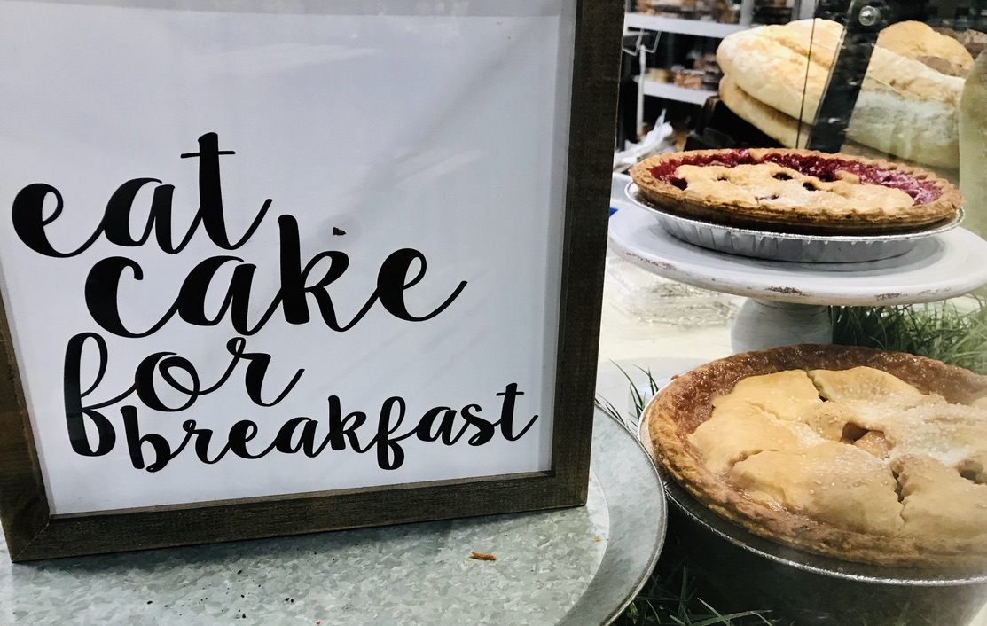 A sign that reads "Eat cake for breakfast" with 2 whole pies off to the side.