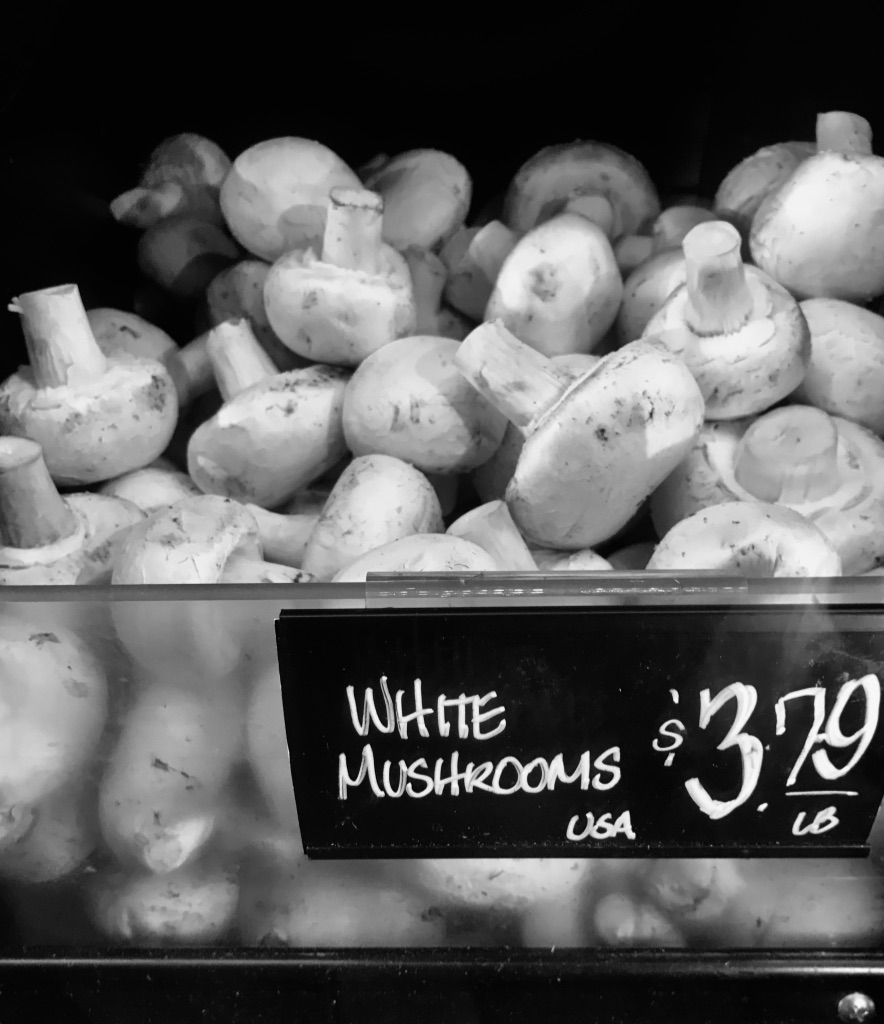 A bin of white mushrooms at a store selling for $3.79 LB.