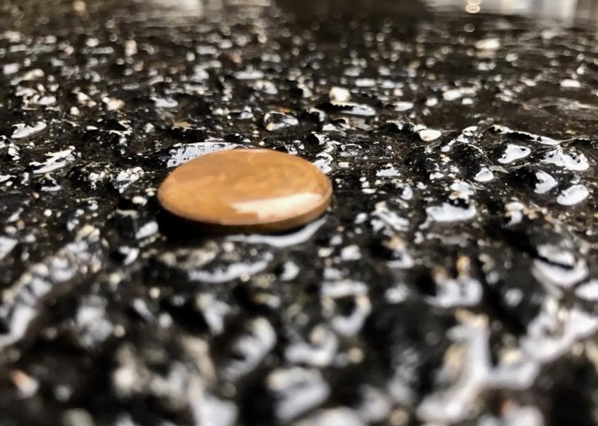 A penny face up on asphalt with a water drop bubble on top. 