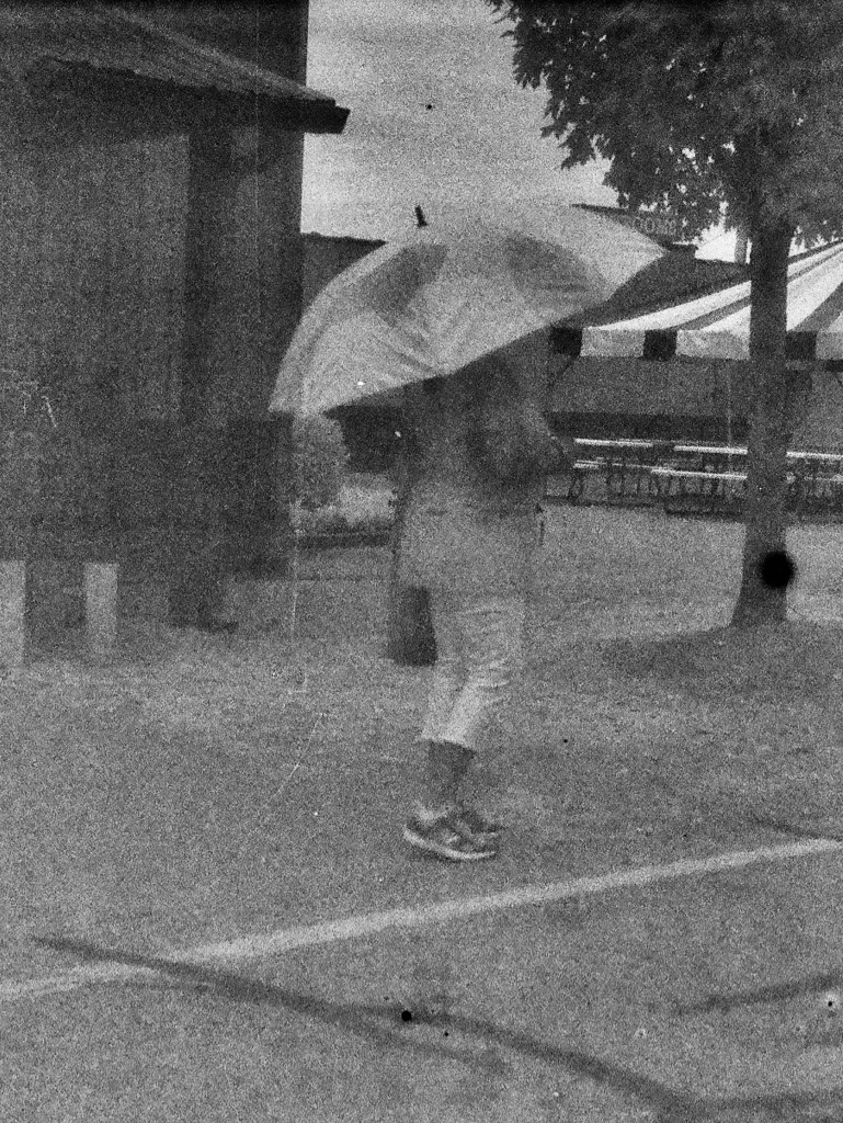 Two photos: 1st is of a women walking with an umbrella down the street.  2nd is looking out a Dr. office window at the street below. 