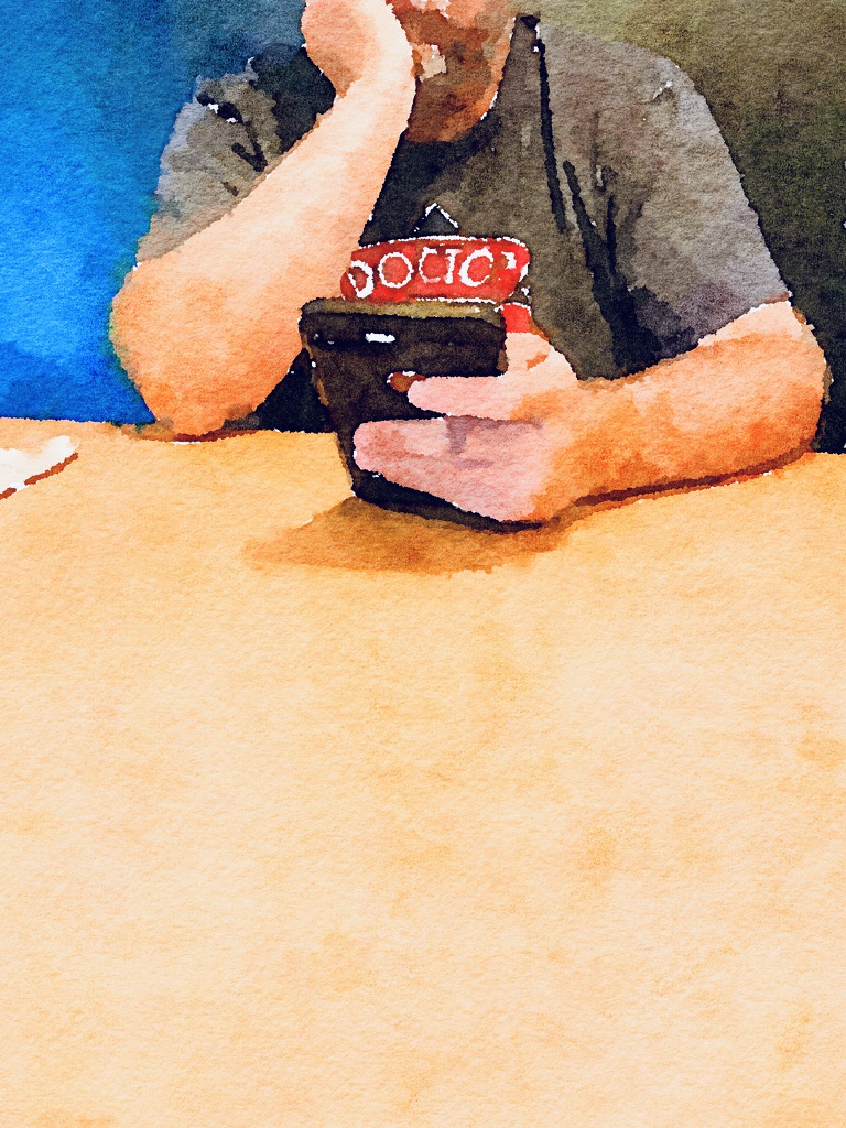 A man from nose down with arms resting on a table looking at a phone.
