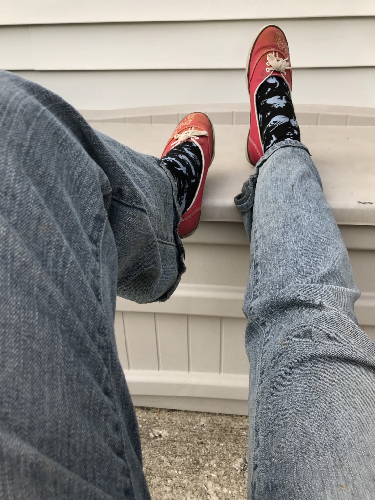 A pair of legs propped up on a plastic chest with red shoes, black socks and old jeans.