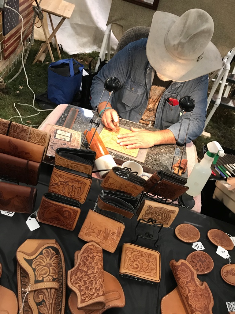 A man in a cowboy hat looking down hand carving leather.