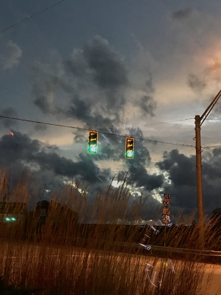Green traffic signals with stormy clouds in background.