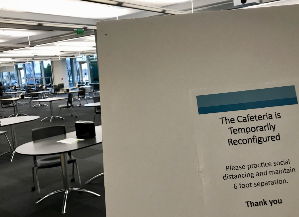 1st photo is a sign that reads "The cafeteria is temporary reconfigured, Please practice social distancing and maintain 6 foot separation". 2nd photo is of the cafeteria with tables all spaced out and only 1 chair per table.