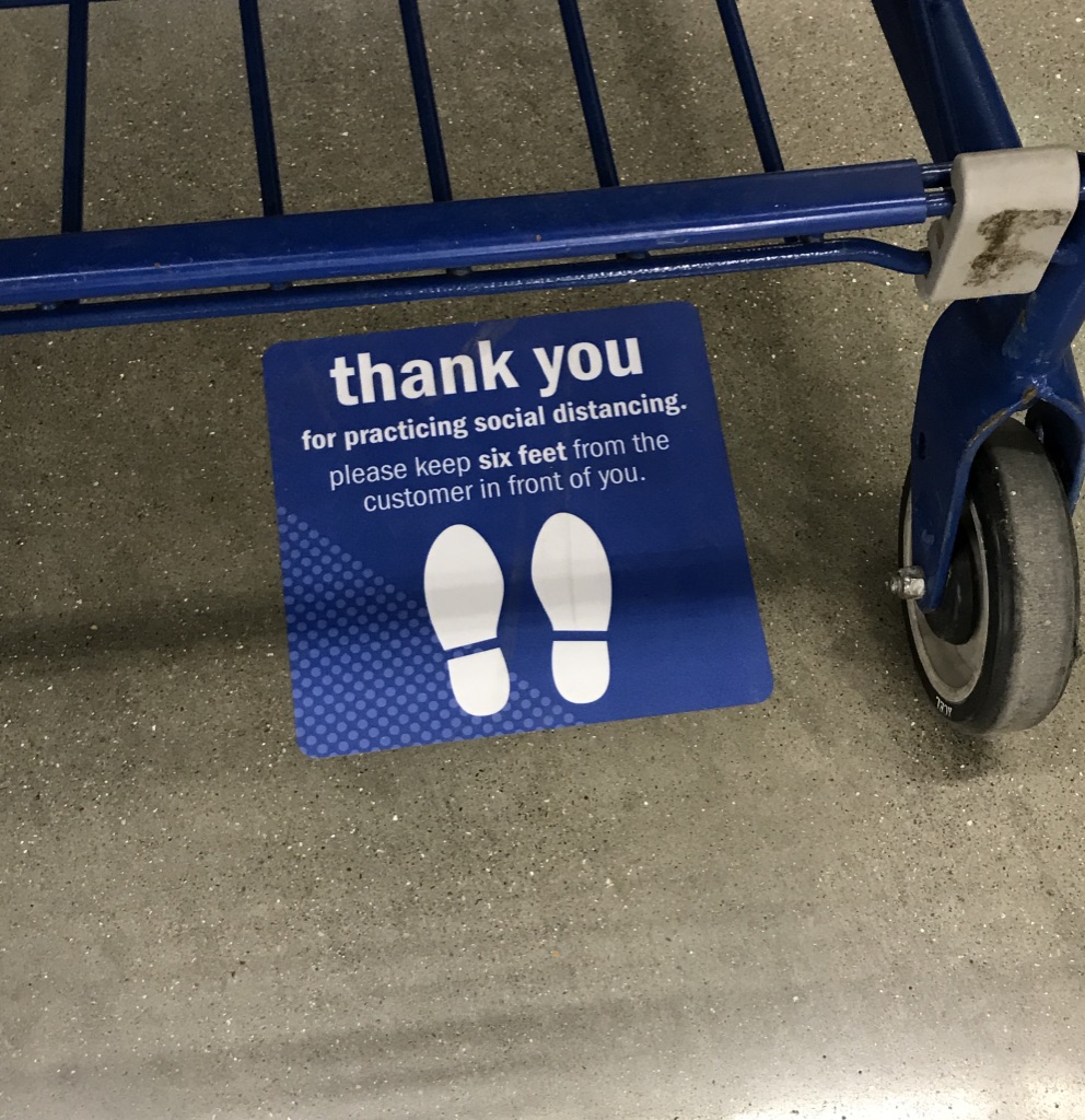 A shopping cart and a sign stuck on the floor that reads "Thank you for practicing social distancing. Please keep six feet from the customer in front of you."